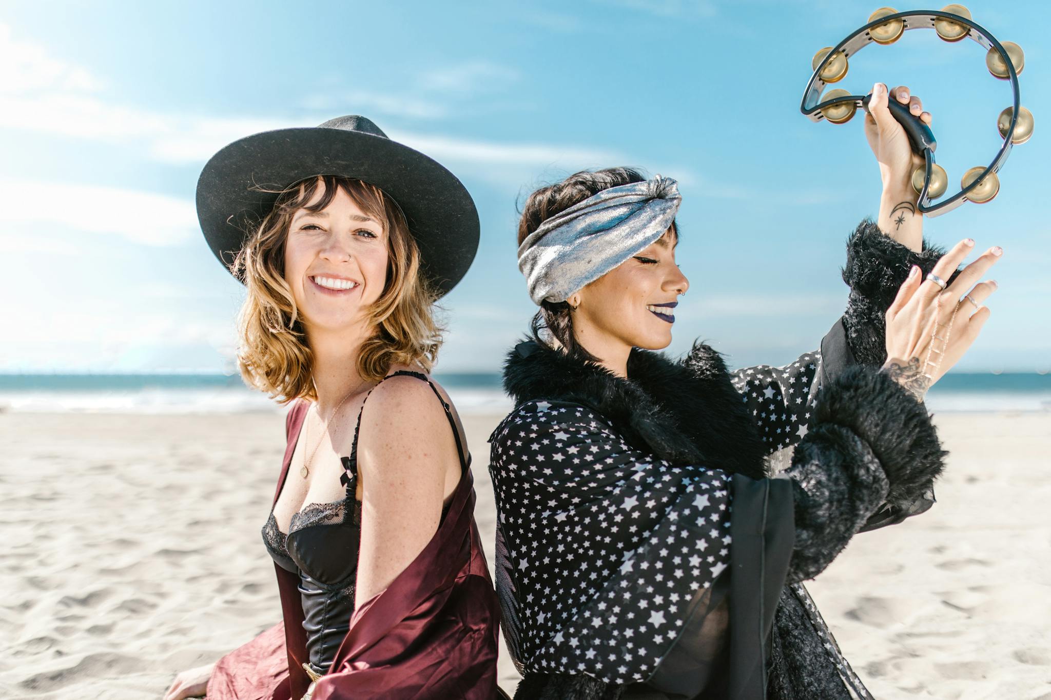 Joyful women at the beach with a tambourine, embracing boho and mystical vibes.